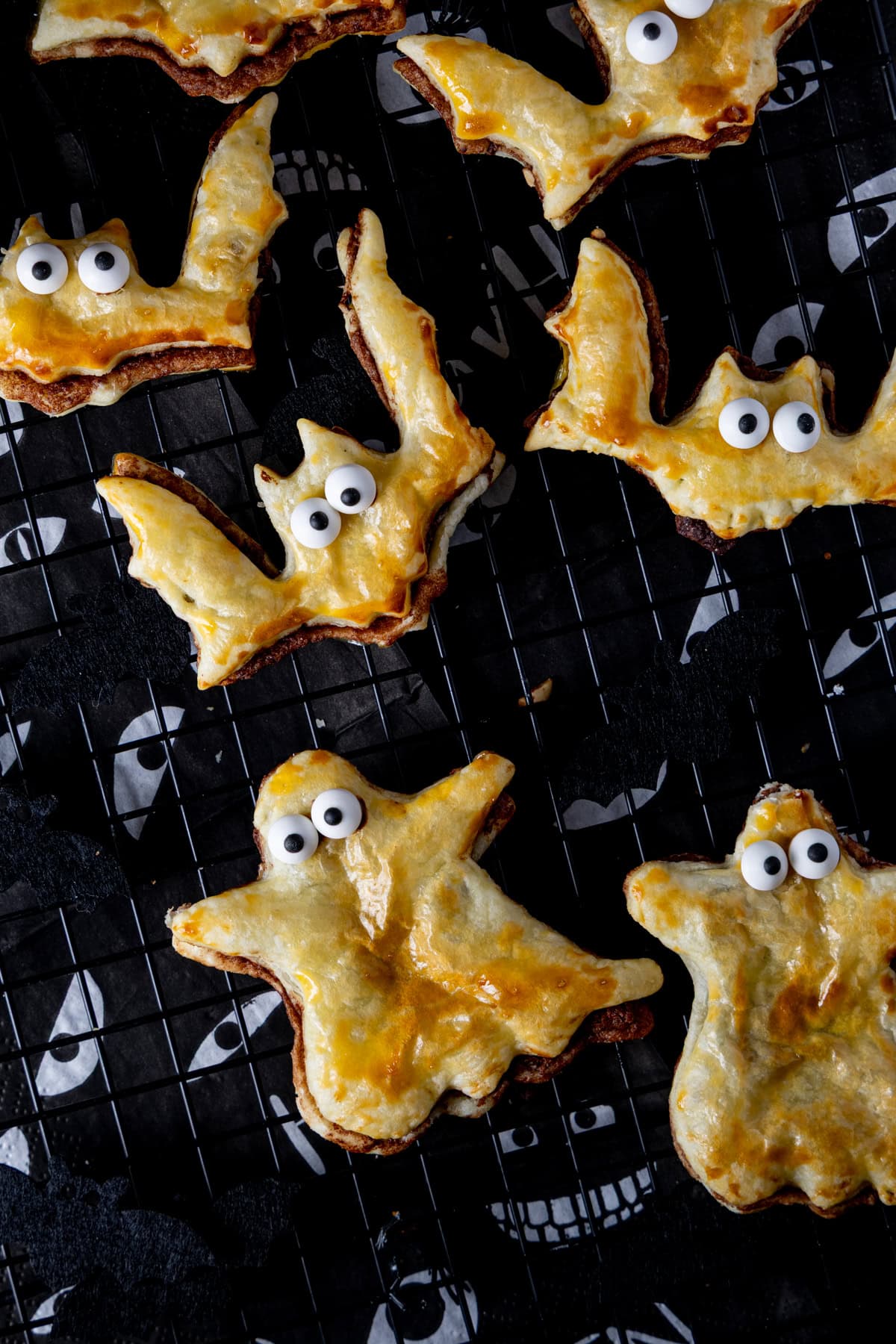 Fledermäuse und Gespenster aus Blätterteig mit Nutella und Haselnüssen gefüllt auf schwarzem Gitter als süße Fingerfood Idee für Halloween.