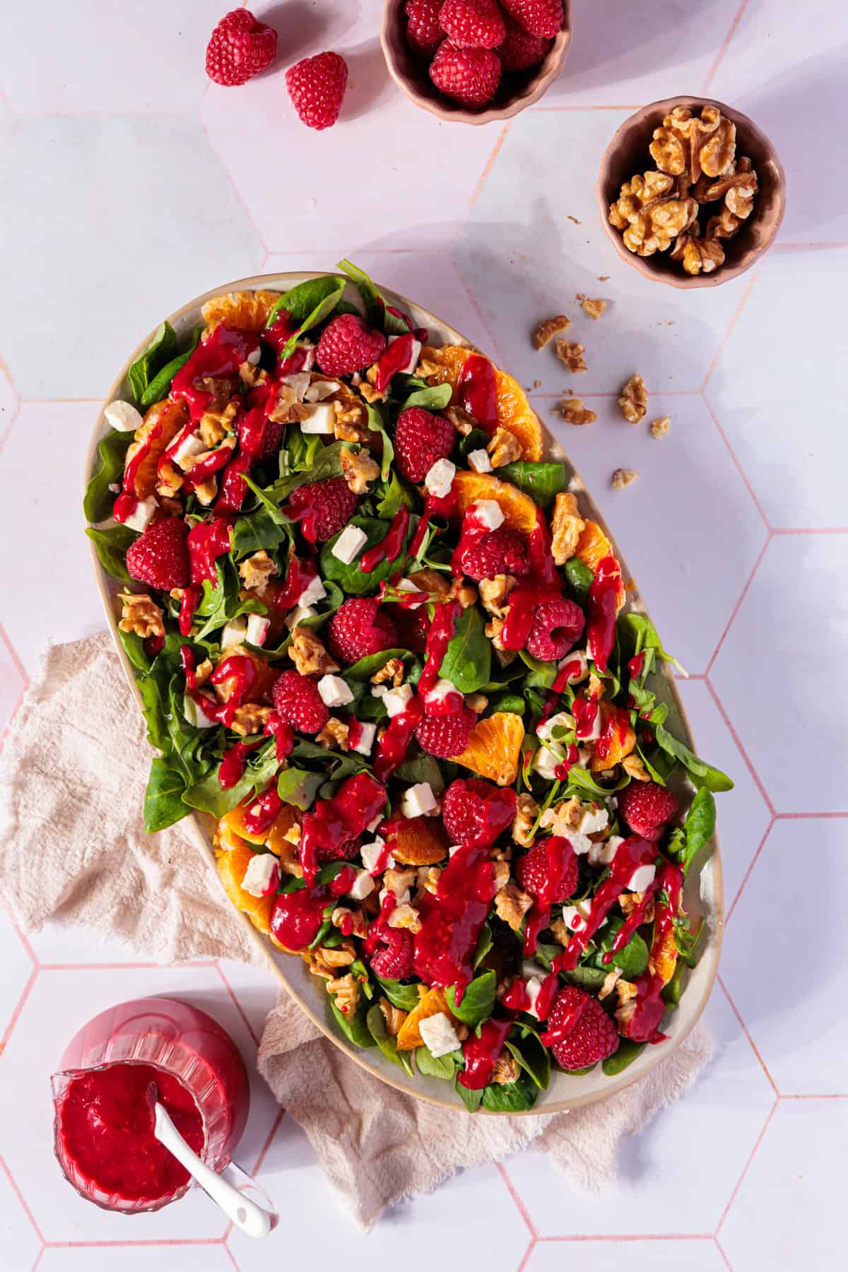 Ein appetitliches Foto präsentiert einen festlichen Wintersalat in einer eleganten Servierschale. Der Feldsalat mit Rucola bildet eine saftige, grüne Basis, die mit leuchtend roten Himbeeren, hellen Feta-Würfeln und goldbraunen Walnussstücken verziert ist. Das Gericht ist großzügig mit einem tiefroten Himbeerdressing beträufelt, das wie ein glänzender Überzug wirkt. Dieser Salat ist perfekt als Vorspeise für Weihnachten geeignet und fängt die festliche Stimmung mit seinen lebhaften Farben und der harmonischen Kombination aus frischen, fruchtigen und herzhaften Elementen ein.