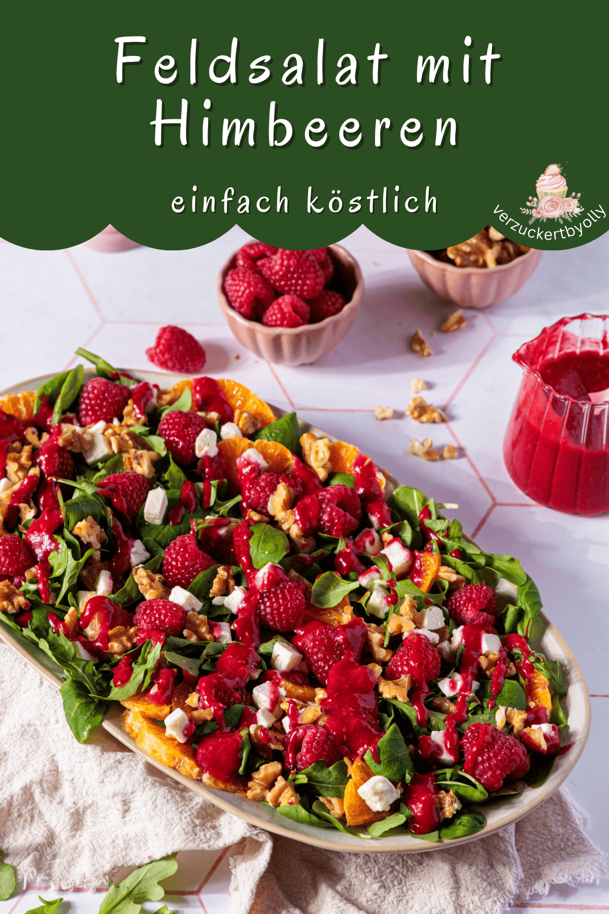 Das Bild zeigt eine ansprechende Aufnahme eines farbenfrohen Wintersalats, ideal als festliche Vorspeise für die Weihnachtszeit. Auf einem länglichen, ovalen Teller ist ein üppiger Feldsalat mit Rucola angerichtet, gespickt mit leuchtend roten Himbeeren, saftigen Orangenfilets, weißen Feta-Würfeln und knackigen Walnüssen. Ein kräftig rotes Himbeerdressing überzieht den gesamten Salat und verleiht ihm eine elegante, glänzende Note. Im oberen Bereich des Bildes ist ein dunkler Banner mit weißer Schrift zu sehen, auf dem "Feldsalat mit Himbeeren einfach köstlich" steht, und ein Logo mit der Aufschrift "verzuckertbyolly". Daneben stehen kleine Schalen mit zusätzlichen Himbeeren und Walnüssen, während ein kleines Kännchen mit dem restlichen Dressing rechts im Bild platziert ist. Die gesamte Komposition strahlt Frische und festliche Eleganz aus.