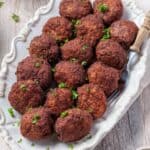 Leckere Frikadellen auf einer weißen Servierplatte, dekoriert mit frischer Petersilie. Das Foto zeigt die saftigen, goldbraun gebratenen Frikadellen, die nach einem einfachen Thermomix®-Rezept zubereitet wurden.