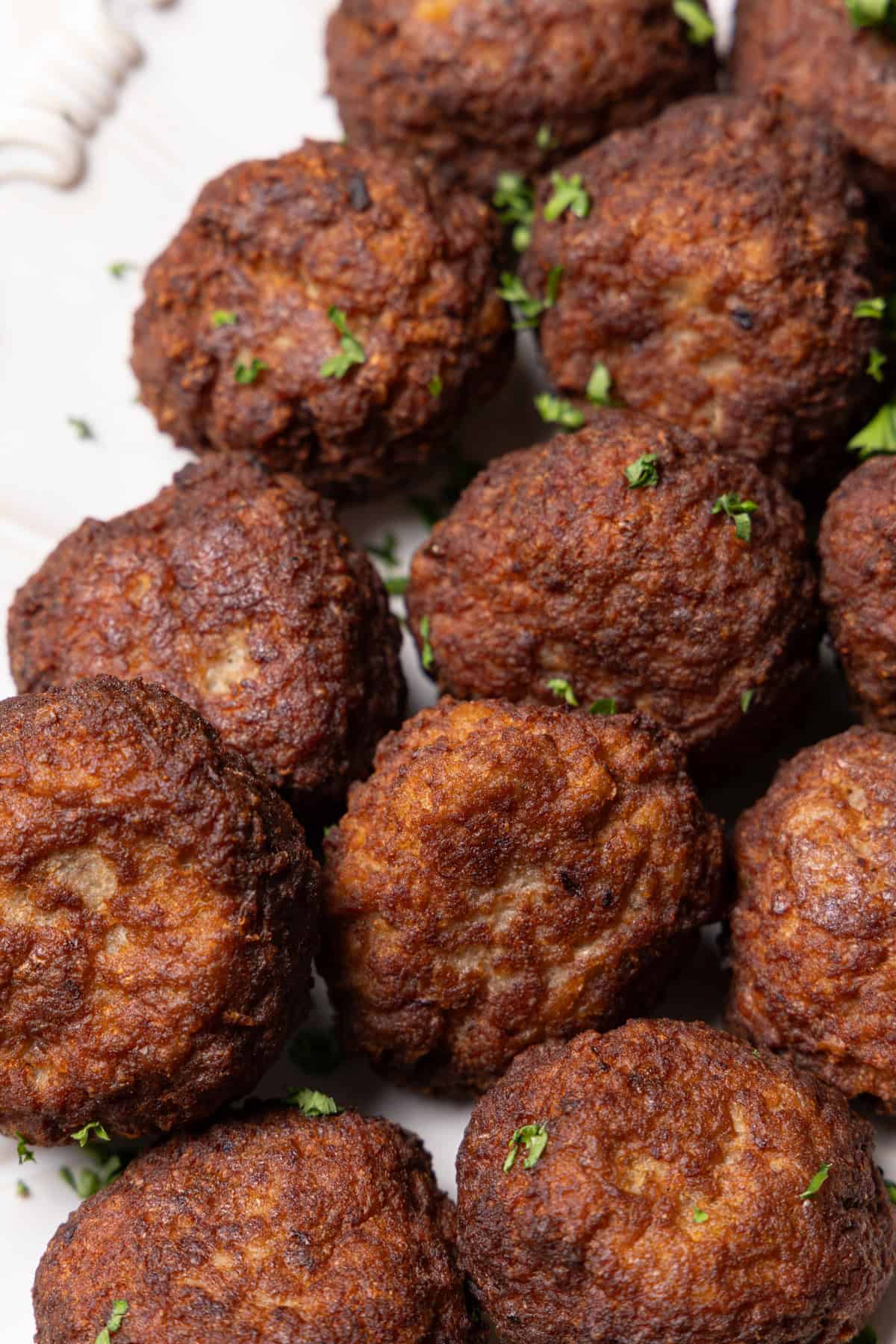 Nahaufnahme von saftigen, goldbraun gebratenen Frikadellen, die appetitlich auf einer weißen Servierplatte liegen. Die Oberfläche der Frikadellen ist knusprig und leicht mit frischer Petersilie bestreut.