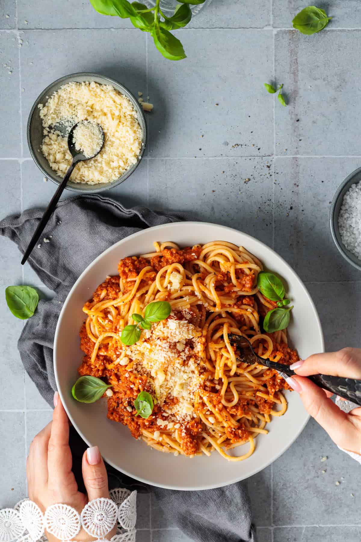 Draufsicht auf einen Teller Spaghetti mit vegetarischer Blumenkohl-Bolognese, der von Händen gehalten wird. Ein gesundes, kalorienarmes Feierabend-Rezept für die ganze Familie. Die fleischlose Pasta ist appetitlich mit Parmesan und Basilikum garniert und ideal für eine schnelle, bewusste Ernährung.